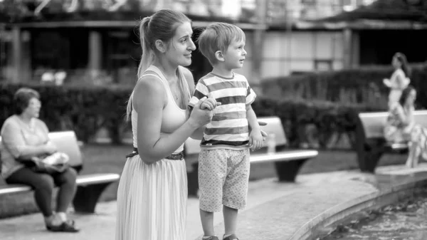 Черно-белое изображение 3-летнего мальчика с улыбающейся молодой мамой в парке — стоковое фото