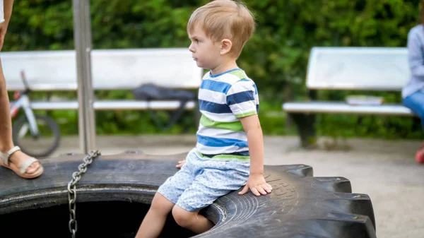 Portret adorable 3-letniego małego chłopca siedzącego na placu zabaw na dużym kole gumowym — Zdjęcie stockowe