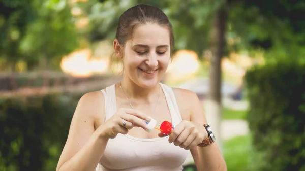 Closeup portrait of beautiful smiling young woman blowing soap bubbles in park at sunset — Stock Photo, Image