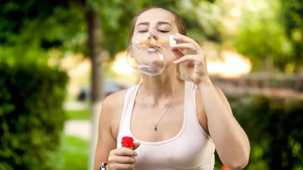 Πορτραίτο του Happy χαμογελαστή νεαρή γυναίκα φυσώντας πολύχρωμες φυσαλίδες σαπούνι στο καλοκαιρινό πάρκο — Φωτογραφία Αρχείου