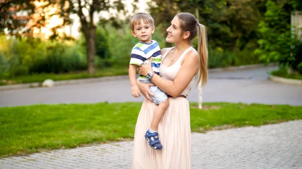 Portret van jonge moederholding en het ondersteunen van haar 3 jaar oude peuter jongen tijdens het wandelen in het Park — Stockfoto