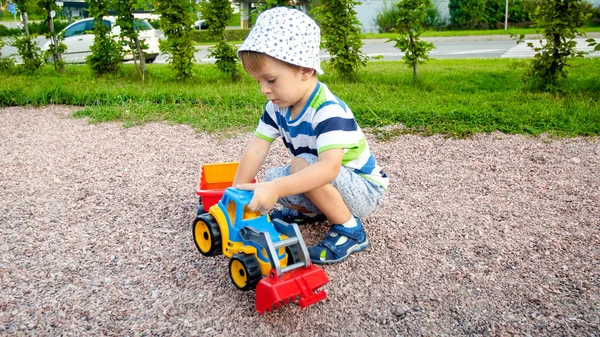 Retrato de un adorable niño de 3 años jugando con un camión de juguete con remolque en el parque infantil. Excavación y construcción de niños desde la arena — Foto de Stock