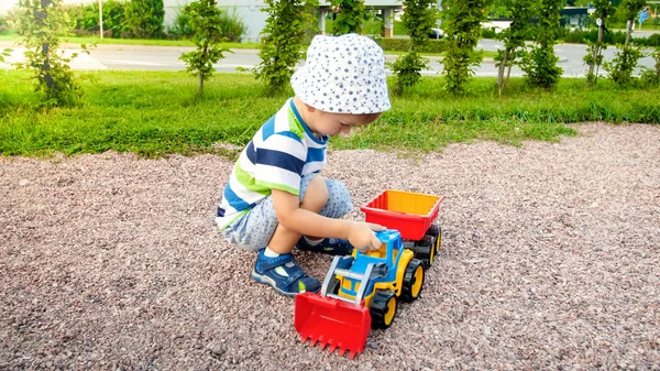 Imagen de primer plano de lindo niño jugando en el palyground con juguetes. Niño divirtiéndose con camión, excavadora y remolque. Está fingiendo ser un constructor o conductor — Foto de Stock