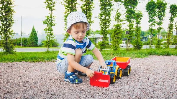 Sevimli 3 yaşındaki yürümeye başlayan çocuk portresi parkta oyun alanında römork ile oyuncak kamyon ile oynarken. Kumdan çocuk kazma ve bina — Stok fotoğraf