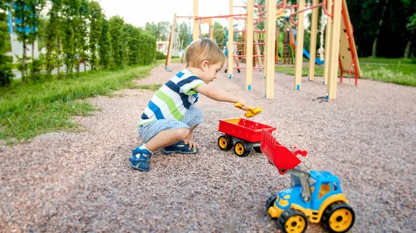 Closeup image of cute little boy playing on the palyground with toys. Child having fun with truck, excavator and trailer. He is pretending to be a builder or driver — Stock Photo, Image