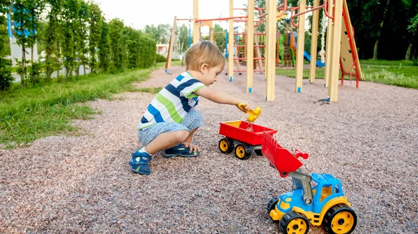 Retrato de un lindo niño de 3 años sentado en el parque infantil y jugando con un colorido camión de juguete de plástico. Niño divirtiéndose y jugando al aire libre con juguetes — Foto de Stock