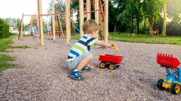 Portrait rapproché d'un enfant souriant de 3 ans creusant du sable sur l'aire de jeux avec un camion ou une pelle en plastique. Palyser les enfants et s'amuser au parc en été — Photo