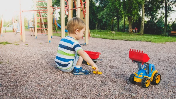 Närbild bild av söt liten pojke som leker på Palyground med leksaker. Barn som har kul med lastbil, grävmaskin och trailer. Han låtsas vara en byggare eller förare — Stockfoto