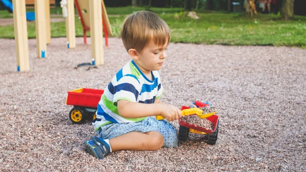 Photo de l'adorable garçon tout-petit de 3 ans jouant avec le sable et vous camion et remorque dans le parc. Enfant creuser et construire dans le bac à sable — Photo