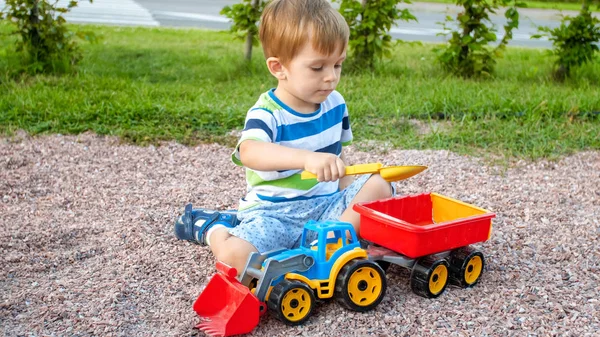 Zdjęcie adorable 3 lat chłopiec maluch gry z piasku i ciężarówki i przyczepy w parku. Kopanie dzieci i budowanie w piaskownica — Zdjęcie stockowe