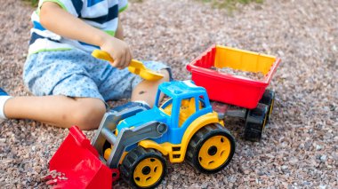 Oyuncaklar ile palyground üzerinde oynayan sevimli küçük çocuk Closeup görüntü. Kamyon, ekskavatör ve römork ile eğlenen çocuk. O bir inşaatçı ya da sürücü gibi davranıyor