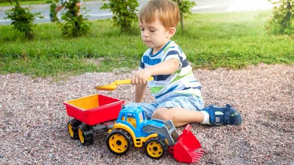 Imagen de primer plano de lindo niño jugando en el palyground con juguetes. Niño divirtiéndose con camión, excavadora y remolque. Está fingiendo ser un constructor o conductor — Foto de Stock