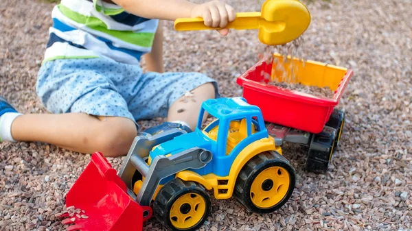 Zdjęcie adorable 3 lat chłopiec maluch gry z piasku i ciężarówki i przyczepy w parku. Kopanie dzieci i budowanie w piaskownica — Zdjęcie stockowe