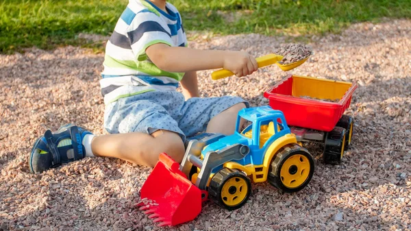 Foto de adorable niño de 3 años jugando con la arena y su camión y remolque en el parque. Excavación y construcción infantil en arenero — Foto de Stock