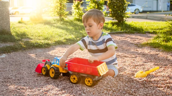 Zdjęcie adorable 3 lat chłopiec maluch gry z piasku i ciężarówki i przyczepy w parku. Kopanie dzieci i budowanie w piaskownica — Zdjęcie stockowe