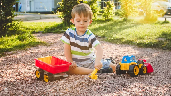 公園の遊び場でトレーラーでおもちゃのトラックで遊ぶ愛らしい3歳の幼児の男の子の肖像画。砂から掘り起こし、建物 — ストック写真