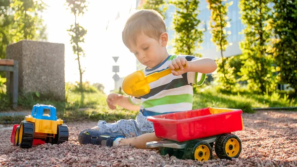 Zdjęcie adorable 3 lat chłopiec maluch gry z piasku i ciężarówki i przyczepy w parku. Kopanie dzieci i budowanie w piaskownica — Zdjęcie stockowe