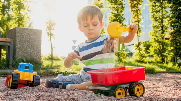 Zbliżenie obraz Cute Little Boy grając na palyground z zabawkami. Dziecko bawią się z ciężarówką, koparką i przyczepą. Udaje mu się być budowniczym lub kierowcą — Zdjęcie stockowe