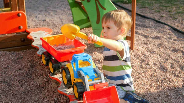 Retrato de niño de 3 años jugando en sandbox con camión de juguete y remolque — Foto de Stock