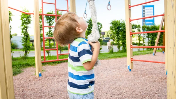 Retrato de 3 años jugando en el patio de recreo y tratando de subir a la cuerda grande en el parque —  Fotos de Stock