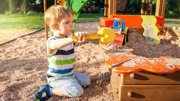 Portrait of cheerful smiling little boy pouring sand in toy truck with trailer. Kids playing and having on playground at park — Stock Photo, Image