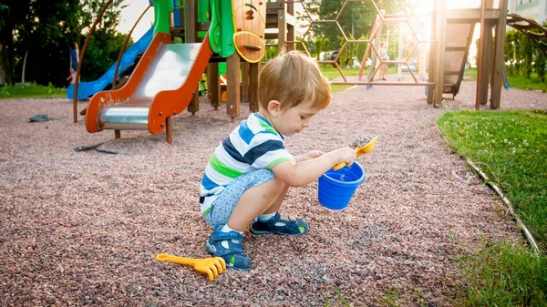 Portret małego 3-letniego chłopca malucha siedzącego na placu zabaw i kopania piasku z zabawką plastikową SPADE — Zdjęcie stockowe