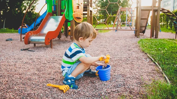 놀이터에 앉아 작은 플라스틱 삽과 양동이와 모래를 파고 사랑스러운 3 살 짜리 소년의 사진 — 스톡 사진