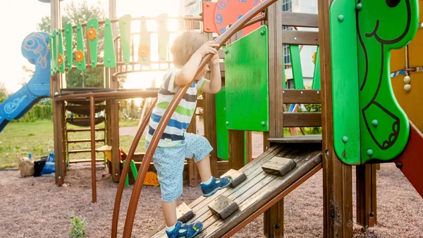Porträt eines entzückenden 3-jährigen Jungen, der auf Leiter auf dem Kinderspielplatz im Park klettert — Stockfoto