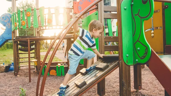 Photo of adorable toddler boy climbing and crawling on wooden staircase on children palyground at park — Stock Photo, Image