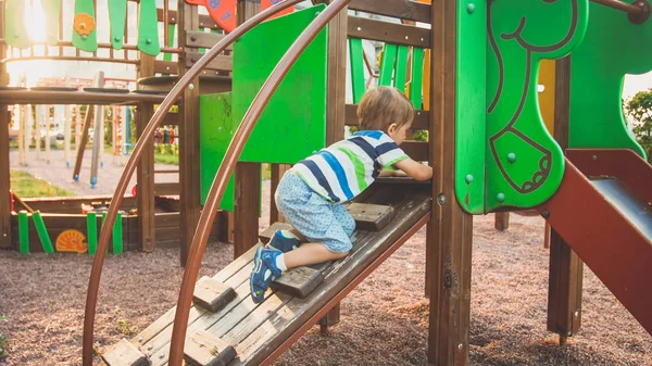 Photo of adorable toddler boy climbing and crawling on wooden staircase on children palyground at park — Stock Photo, Image