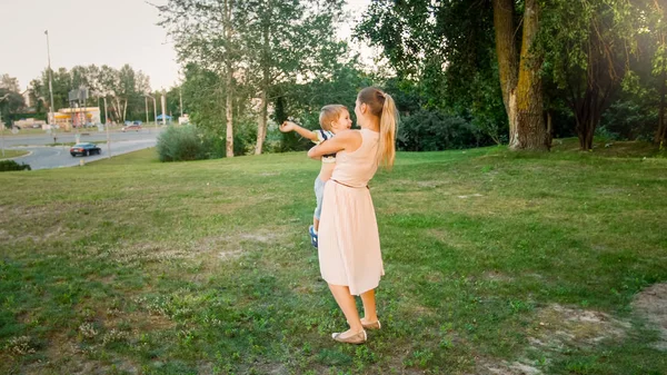 Tónový obraz šťastné usmívající se mladé matky, držící v parku svého batole syna — Stock fotografie