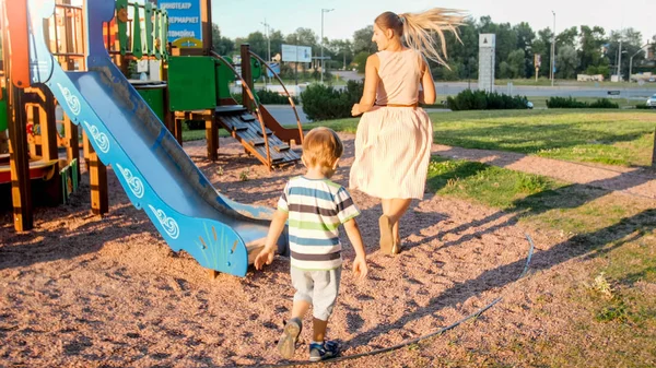 公園の遊び場を歩いて走っている若い母親と幸せな陽気な幼児の少年の写真 — ストック写真