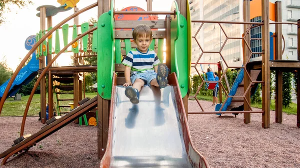 Zdjęcie adorable uśmiechnięty chłopiec wspinaczki i jazdy na slajdzie. Aktywne dziecko bawią się i bawią w parku — Zdjęcie stockowe