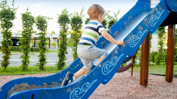 Obraz szczęśliwy uśmiechnięty wesoły chłopiec jazda konna i wspinaczka na duży plac zabaw dla dzieci w parku — Zdjęcie stockowe