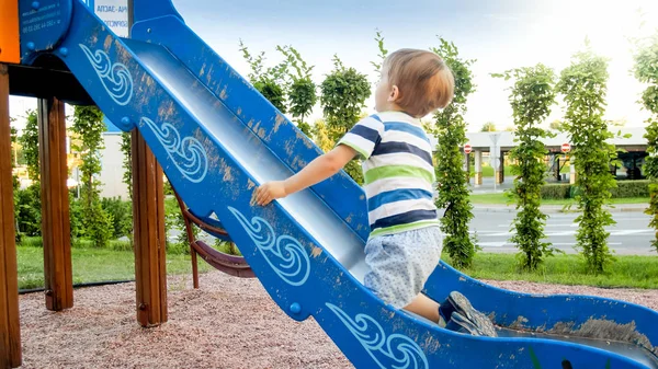Zdjęcie adorable uśmiechnięty chłopiec wspinaczki i jazdy na slajdzie. Aktywne dziecko bawią się i bawią w parku — Zdjęcie stockowe