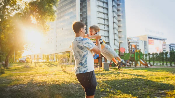 Retrato de feliz jovem pai abraçando e girando seu pequeno filho sorridente no parque — Fotografia de Stock