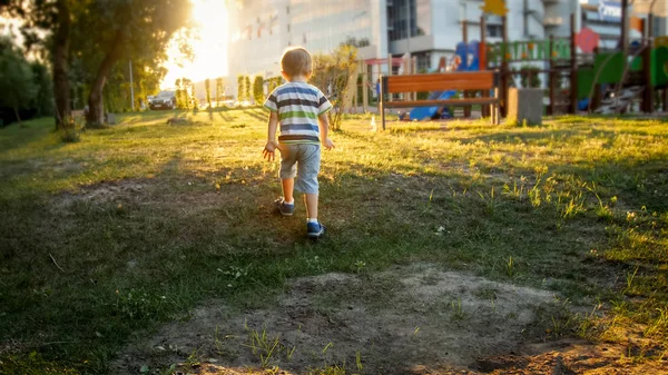 Фото маленького мальчика, бегущего по траве в парке на фоне красивого закатного неба — стоковое фото
