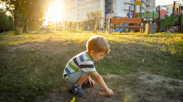Photo of cute little toddler boy sitting in park and digging sand — Stock Photo, Image