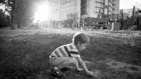 Photo of cute little toddler boy sitting in park and digging sand — Stock Photo, Image