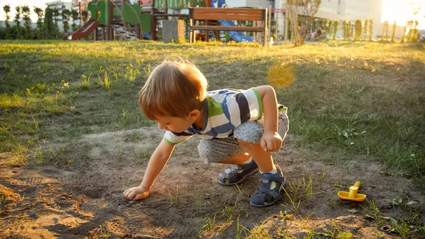 Sevimli küçük yürümeye başlayan çocuk parkta oturan ve kum kazma fotoğrafı — Stok fotoğraf