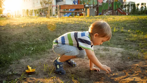 Foto von 3-jährigem kleinen Jungen, der auf dem Boden im Park sitzt und Sand gräbt — Stockfoto