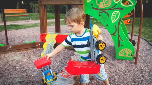 Stonowane zdjęcie Cute Little Boy chłopiec gry z ciężarówki zabawki i przyczepy na placu zabaw w parku — Zdjęcie stockowe