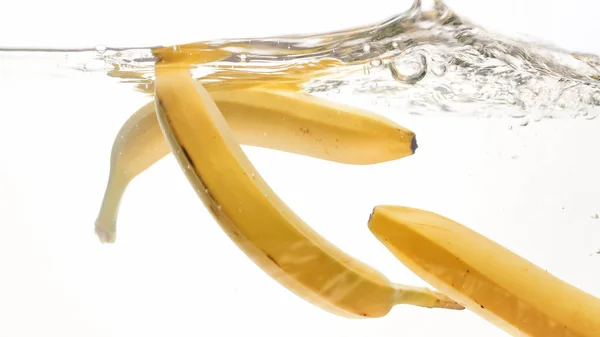 Εικόνα σε κοντινό πλάνο φρέσκων ώριμων μπανανών που πέφτουν και πιτσιλίσματα στο νερό από το λευκό απομονωμένο φόντο — Φωτογραφία Αρχείου