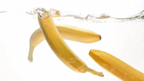 Κοντινό πλάνο φωτογραφίες φρέσκων φρούτων που πέφτουν στο νερό. Κίτρινο γλυκό babanas πιτσίλισμα και ρέει στο νερό από λευκό φόντο — Φωτογραφία Αρχείου