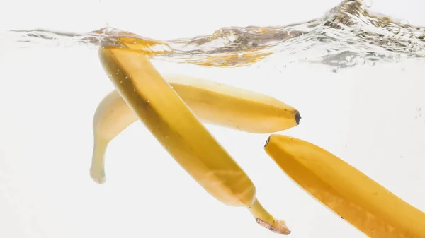 Κοντινά πλάνα όμορφη εικόνα των μπανανών που πέφτουν σε καθαρό νερό από λευκό φόντο, πολλές φυσαλίδες αέρα flaoting και πιτσιλίσματα νερού — Φωτογραφία Αρχείου