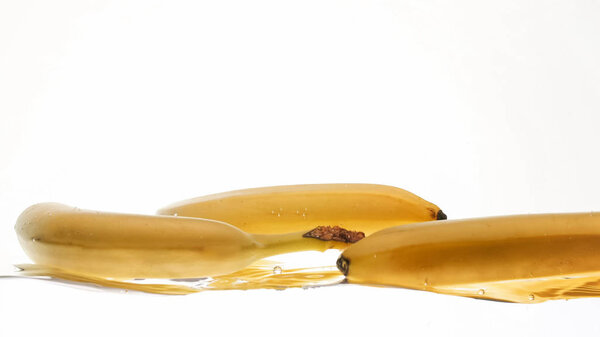 Closeup image of fresh ripe bananas falling and splashing in water against white isolated background