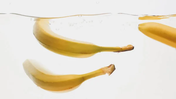 Imagem de close-up de bananas maduras frescas caindo e salpicando na água contra fundo isolado branco — Fotografia de Stock