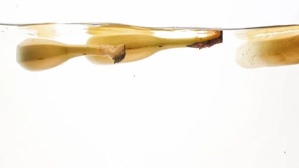 Closeup bela imagem de bananas caindo em água clara contra o fundo branco, muitas bolhas de ar flaoting ar e salpicos de água — Fotografia de Stock