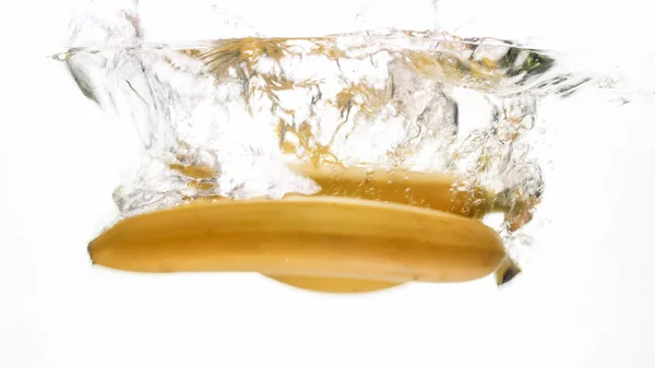 Imagem de close-up de bananas maduras frescas caindo e salpicando na água contra fundo isolado branco — Fotografia de Stock