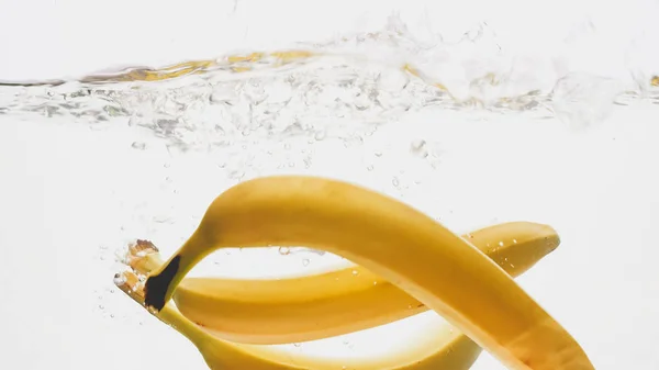 Foto de close-up de bananas amarelas maduras frescas caindo e salpicando em água clara contra o backgorund branco isolado — Fotografia de Stock